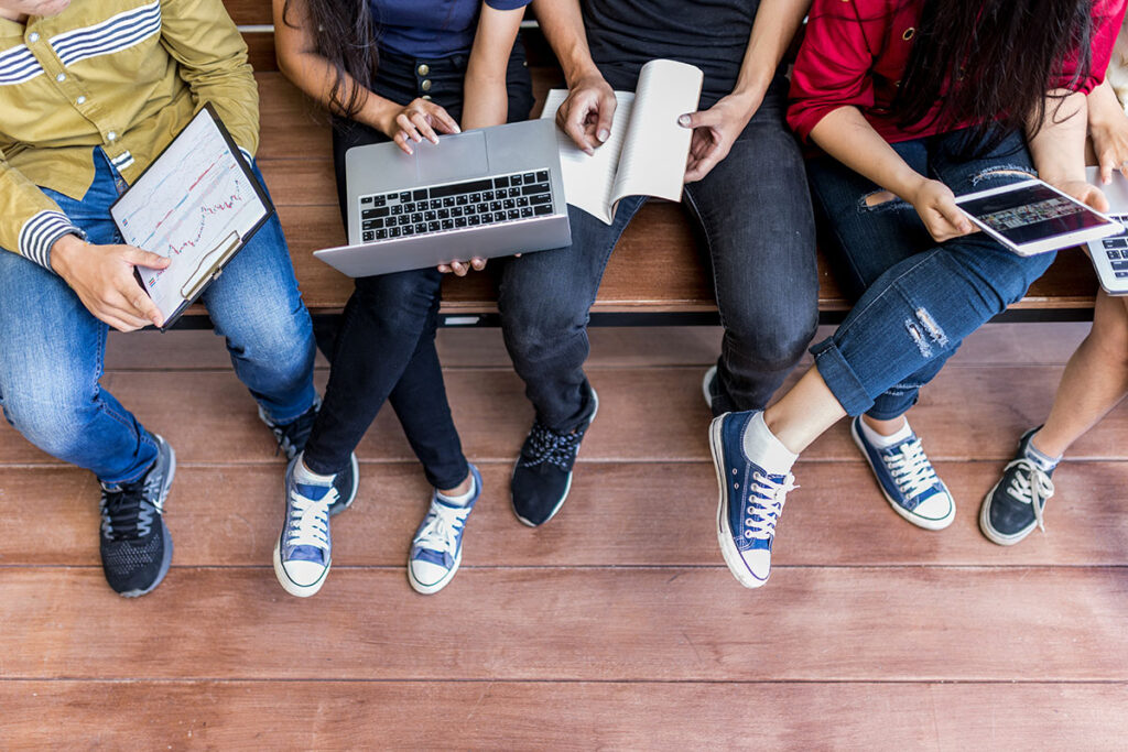college students sitting on bench holding electronic devices
